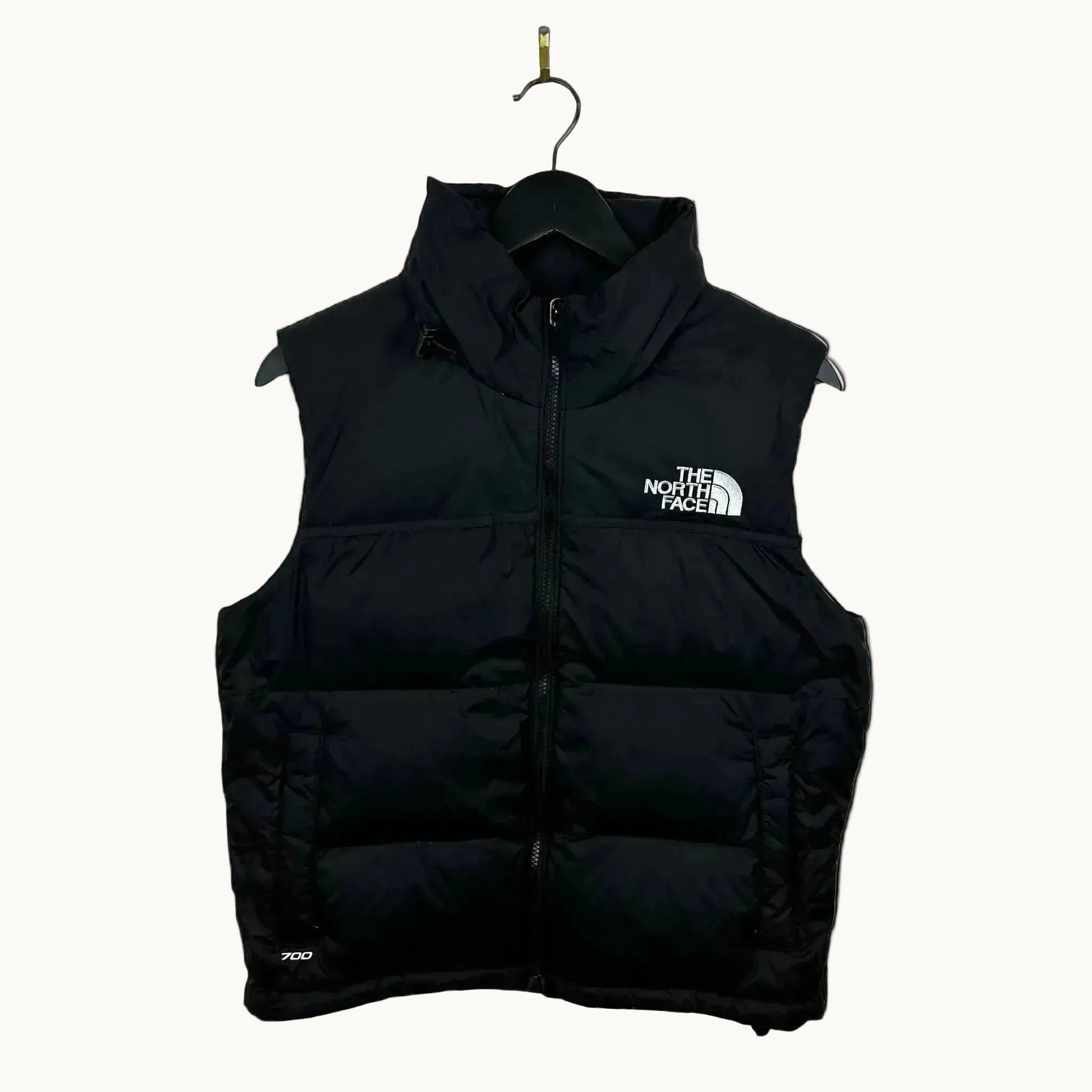 Black puffer vest with The North Face logo on a beige background