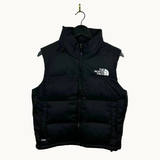 Black puffer vest with The North Face logo on a beige background